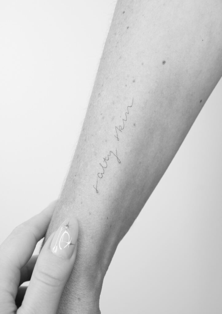 black and white Close up to an arm with a line saying salty skin in minimal drawing style